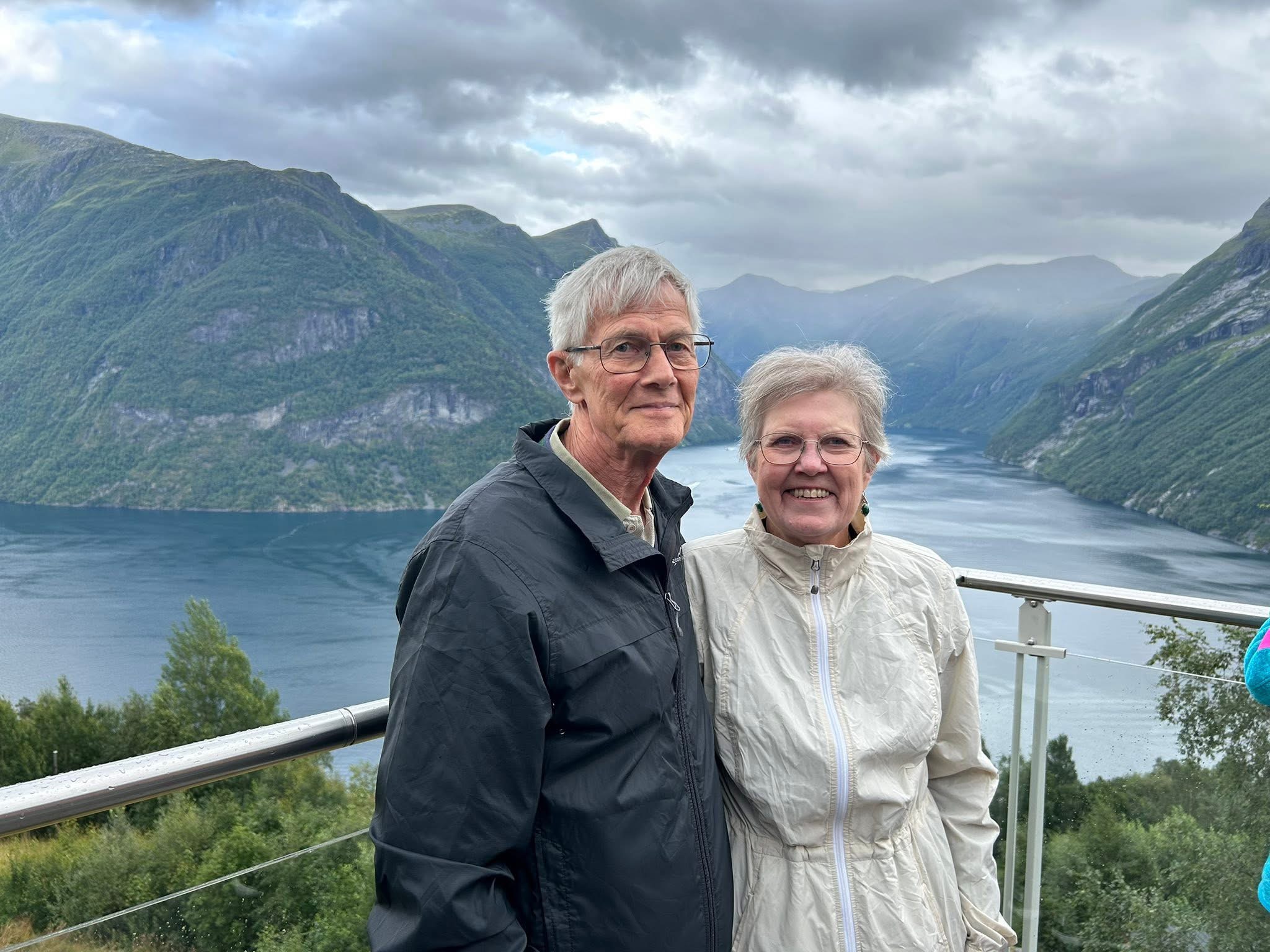 Pictured: Ron and wife Karen standing on a lookout facing the camera with a river and mountains in the background